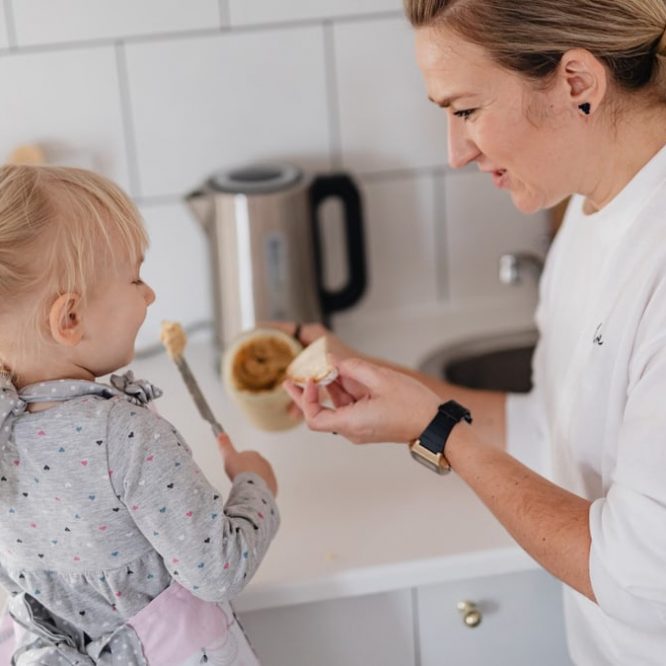 A mother and her young daughter interact while preparing food in a modern kitchen.