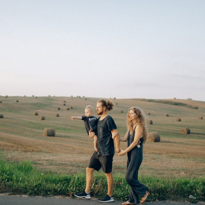 A joyful family walking hand in hand across a picturesque hayfield landscape at sunset.